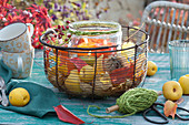 Tealight holder in a wire basket with autumn leaves, ornamental quinces, rose hip and chestnut