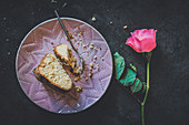 A slice of coconut Bundt cake with cinnamon on a plate next to a long-stemmed rose