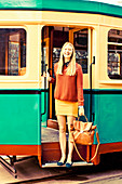 A young blonde woman wearing a jumper and a skirt standing in the door of a tram