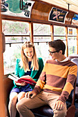 Junges Paar mit Buch im Pullover, Hose, Rock und Jacket sitzt im Bus
