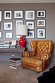 Vintage leather armchair and console table with table lamp and books against gray wall with photo gallery