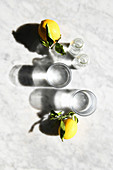 Frische Zitronen und zwei Wassergläser im Sonnenlicht (Aufsicht)