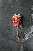 Antipasto meat assorti of sliced jamon, salami, chorizo sausage on fork over black marble background