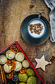 A cup of Turkish salep garnished with cinnamon powder, box full of cookies, cinnamon sticks and orange chips