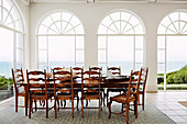 Long table with wooden chairs in front of arched window fronts with sea view