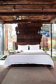 Bed against wall made of wooden planks in the bedroom with louvre windows