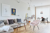 Pale grey sofa, coffee table and pink armchair in front of dining area in bright, open-plan interior
