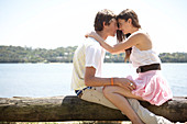 Junges Paar auf Baumstamm sitzend am See