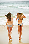 Zwei Frauen in Bikinis und mit Sommerhut an einem Strand