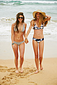 Two women wearing bikinis and summer hat on the beach