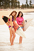 Two women on a beach with surfboards wearing bikinis