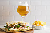 Delicious sandwich with ham, cheese, lettuce and tomato with a glass of beer and chips