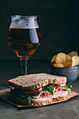 Delicious sandwich with ham, cheese, lettuce and tomato with a glass of beer and chips