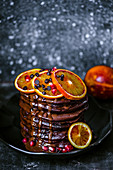 Chocolate pancakes with chocolate drops, sprinkled with chocolate sauce, decorated with slices of red oranges
