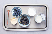 Food tray with blueberries, black raspberries, yogurt jar, tartlet cases, a glass and a spoon