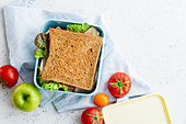 Healthy sandwich with greens, ham, tomatoes and cheese packed in plastic container