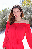 A brunette woman outside wearing a red off-the-shoulder dress
