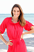A brunette woman by the sea wearing a red dress