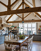 Wooden table in large, country-house-style kitchen-dining room with exposed roof structure