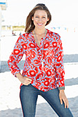A blonde woman on a beach wearing a tunic with a floral pattern and jeans