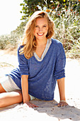 Junge Frau in Shorts und blau meliertem Shirt sitzt am Strand