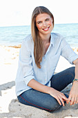 A young woman by the sea wearing a light blue shirt and jeans