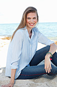 A young woman by the sea wearing a light blue shirt and jeans