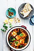 A pan with baked chickpeas in tomatoe sauce with kale and tofu. Vegan dish served with chapati bread