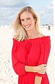 Blonde Frau in rotem Kleid am Strand