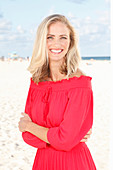 A blonde woman on a beach wearing a red dress