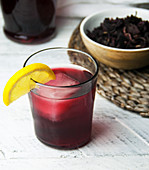 A glass of cold Sorrel drink with lemon wedge garnish with sorrel leaves in bowl