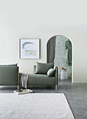 Reduziert eingerichteter Wohnraum in Grau-Weiß mit Sofa und Rundbogendurchgang