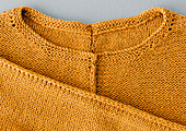 A yellow-orange, hand-knitted jumper with a middle seam