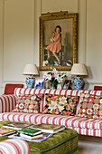 Antique painting above striped sofa with tapestry scatter cushions in English manor house