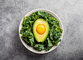 A raw egg yolk in a halved avocado on a bed of kale