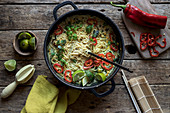 Green curry pasta with limes, herbs and chili pepper in pot on wooden background