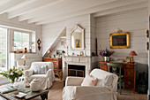 Weiße Hussensessel und Couchtisch auf Rädern vor Kamin im Wohnzimmer mit weiß gestrichenen Holzwänden