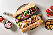 Variety of beef baguette sandwiches with champignon mushrooms, green salad, fried onion and tomatoes