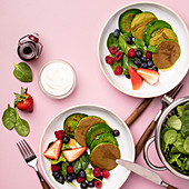 Spinach pancakes with fruits and vegetables on pink background