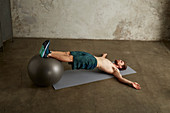 A young man lying on his back with his feet on a gym ball