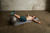 A young man lying on his back with his feet on a physio ball and buttocks on the floor
