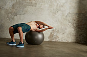 A young man lying on his back on a physio ball with his arms stretched to the side