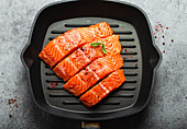 Fresh raw salmon fillet garnished with green basil leaves on grill skillet