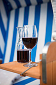 A glass of red wine and a carafe of wine in a beach chair