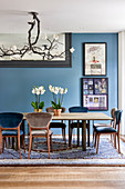 Magnolia light fitting above dining table with orchids and artworks on blue wall