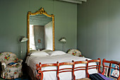Antique bench at foot of bed below gilt-framed mirror in bedroom
