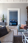 View through double doors into bedroom with grey-blue walls, bed and bedroom bench