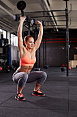 A young woman performing an air squat with dumbbells in both hands
