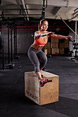Junge Frau steht auf Holzkiste bei Fitnessübung Pistols (einbeinige Kniebeugen)