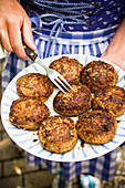 A woman holding a plate of meat patties